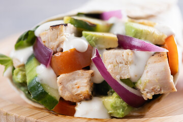 A delicious grilled chicken wrap with vegetables on wooden table. Close up