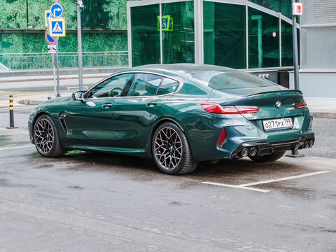 Green car BMW M8 Competition parked in front of modern glass office building