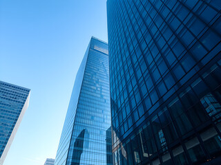 Glass and steel skyscrapers under blue sky, modern urban architecture with reflective surfaces, wide shot with compressed perspective, f/8.0, even 