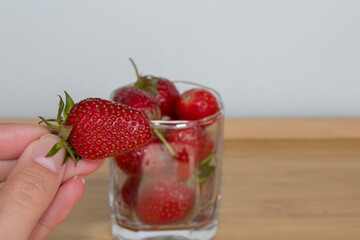 Hand holding a strawberry from cup full of the same fruit.