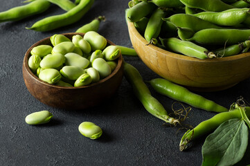 Fresh broad beans with pod in bowl on dark rustic background, healthy food