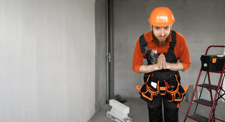 Bearded repairman or builder in protective helmet and overalls begging for mercy being disappointed...