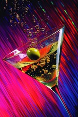 Dynamic pop art style image of a tilted martini glass with an olive and vibrant splash against a neon striped background