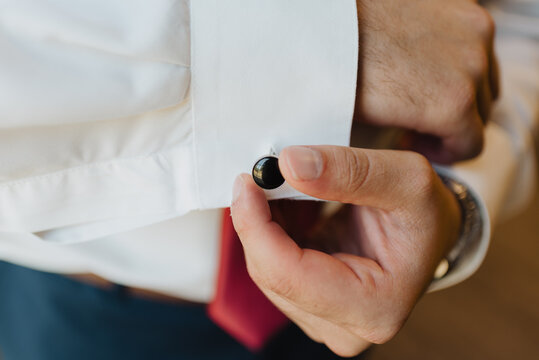 Close up of man fastening black cufflink on white dress shirt, elegant men’s fashion accessory detail, groom or businessman getting ready, formalwear style concept with natural light