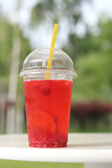 Lemonade in a disposable plastic cup, takeaway drink. Refreshing drink against the background of a park in summer. Pink lemonade with raspberries and lime. Close-up of a drink in a disposable cup