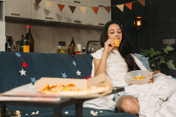 Young woman eating potato chips on sofa after house party