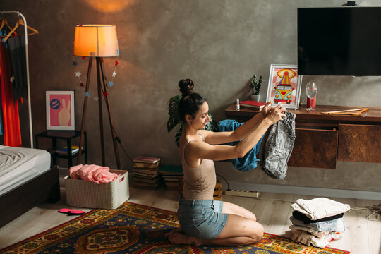 Young woman tidying up clothes in bedroom after party