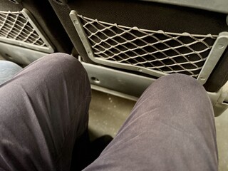 Two passengers are sitting in an armchair with a narrow footway in the economy class cabin of the bus. View of the legs from above. People in transport, close-up