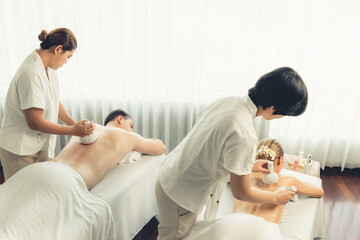 Hot herbal ball spa massage body treatment, masseur gently compresses herb bag on couple customer...