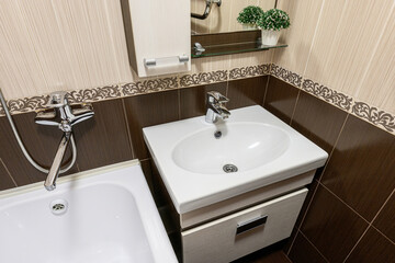 bright bathroom corner features a white sink vanity, a bathtub, and beige brown tiles with decorative trim