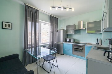 small, modern kitchen with turquoise walls, blue cabinets, and gray accents. A glass table sits by...