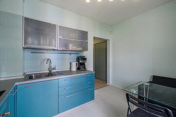 bright kitchen with light blue cabinets, stainless steel appliances, and a glass table. The room is clean and well-lit