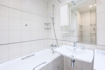 Bright, clean bathroom featuring white tiles, a bathtub, sink, and a mirrored cabinet