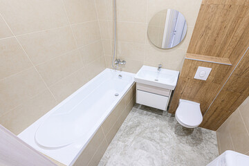 clean, modern bathroom with beige tiles, a white bathtub, a sink with a cabinet, a round mirror,...