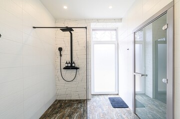 Bright bathroom with white tiled walls, a walk-in shower featuring a black shower system, and a...