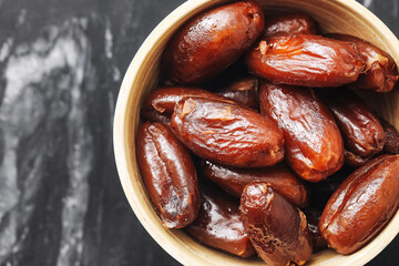 Natural dried dates in black bowl. Sweet brown exotic fruit closeup. Organic healthy snack rich in fiber. Traditional Ramadan food. Tasty dessert ingredient. Rustic kitchen marble background.