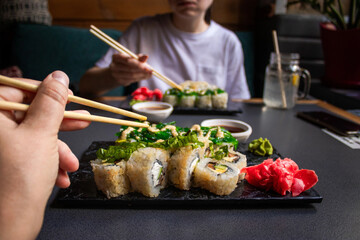 Closeup hand holding bamboo chopsticks with nigiri shrimp while soaking it in soy sauce. Detail of sushi set on wooden tray at restaurant while hand dip nigiri in soy sauce. Japanese cuisine concept.