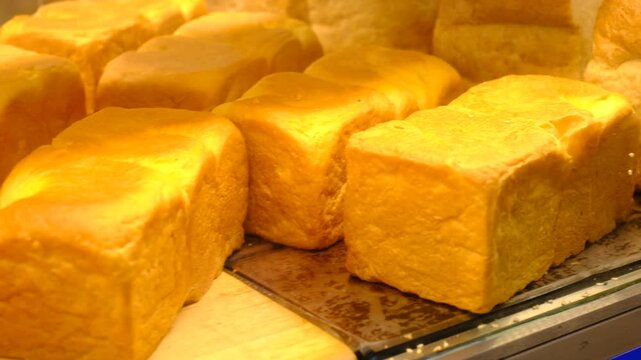 A row of bread loaves are displayed on a counter. The bread is golden brown and he is freshly baked
