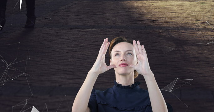 Woman wearing dark blouse positioning hands around interface in studio, with network graphics