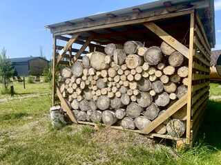Neatly stacked firewood in a rustic wooden log holder in a rural countryside backyard on a warm summer day. Traditional woodpile storage in village. Cozy natural eco-friendly lifestyle