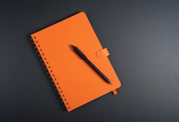 Orange notebook and pen on dark surface for writing and note taking concept