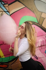 Young woman enjoying cotton candy against vibrant street art backdrop in an urban setting