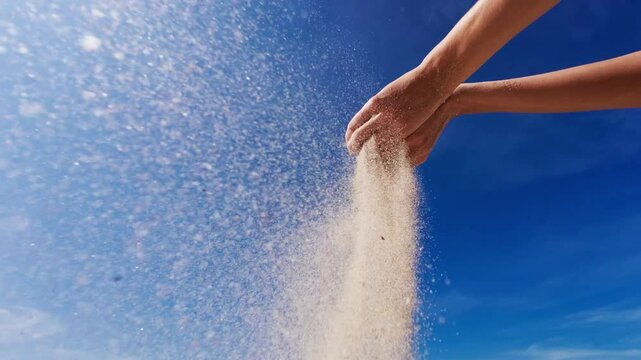 Woman pouring sand from hand on beach, blue sky.