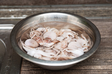Raw baby octopus in metal bowl for cooking. Close-up of fresh baby octopus soaking in water inside a stainless steel bowl, ready for seafood preparation or cooking.