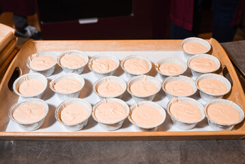 Unbaked cupcake batter in foil baking cups. A tray filled with foil baking cups containing light brown cupcake or muffin batter, ready to be placed in the oven.