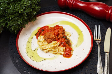 Italian tagliatelle with meatballs and tomato sauce. Plate of tagliatelle pasta served with meatballs in tomato sauce, garnished with herbs and olive oil, ready to eat.