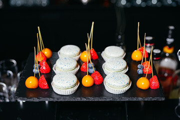Gourmet macarons with fruit skewers on display. Elegant dessert display featuring blue-speckled macarons and colorful fruit skewers with strawberries, blueberries, and golden berries.