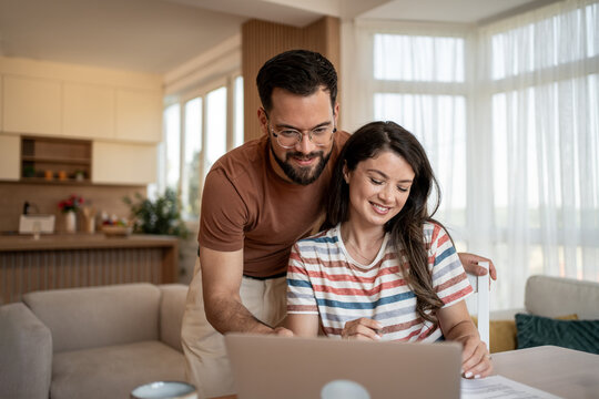 Happy couple managing domestic finances with laptop at home