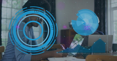 Woman and mature man collaborating in bright office, using tablet and laptop with charts overlay