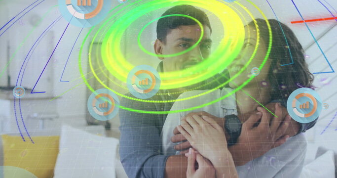 Embracing couple sitting on sofa at home, with digital overlay of bar chart icons