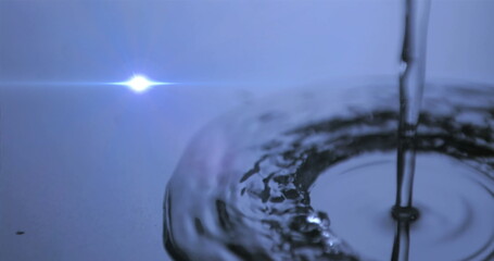 Pouring water stream creating ripples on reflective surface in studio, with lens flare, copy space