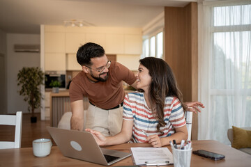Happy couple smiling and using laptop at home for finances