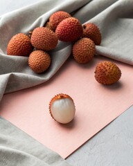 Peeled and whole lychee fruit displayed on pastel paper against a soft grey background for artistic photography.