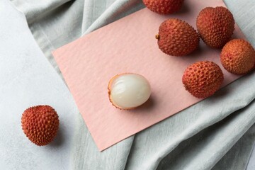 Peeled and whole lychee fruit arrangement on soft grey pastel paper for artful display and photography.