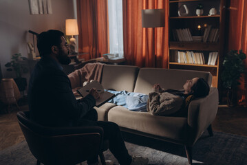 Obraz premium Bearded man therapist with notebook and pen in hands consults female patient