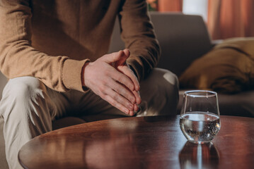 Man sits on couch near table with glass of water expressing feelings