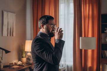 Bearded man psychologist sips water from glass standing in therapy room