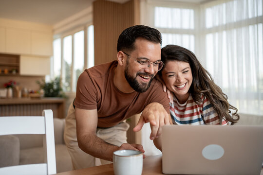 Happy couple laughing and browsing internet on laptop at home - Powered by Adobe