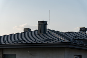 Fototapeta premium A contemporary house rooftop features sleek metal chimneys and angled panels, set against a bright sky during daytime hours