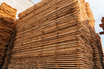 Large piles of lumber are neatly stacked in a yard, showcasing various lengths and widths of wooden planks under a bright sky