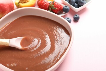 Baby food. Eating tasty puree with spoon at pink table, closeup