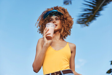 Young woman enjoying a refreshing drink in a sunny outdoor setting with palm trees in the background
