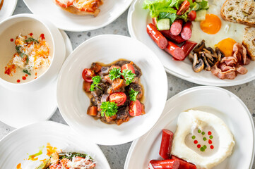 Assorted dishes including creamy soup, beef stew with tomatoes, English breakfast, and mashed potatoes with sausages, served on a rustic wooden table.