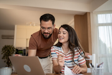 Happy couple working from home having fun using laptop computer