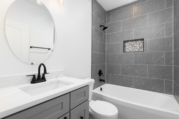 A bathroom with a grey vanity cabinet with a white marble countertop, white walls, and a tiled...