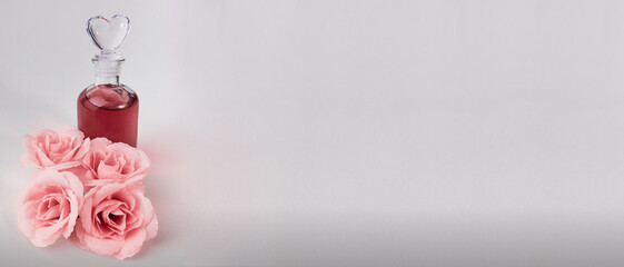 Closeup of a glass bottle of perfume with artificial pink roses on the white background